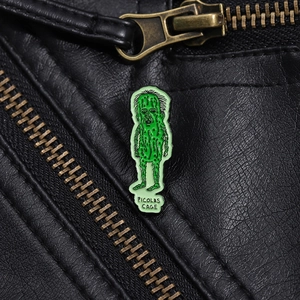 Macro shot of green bitter melon enamel pin with Picolas Cage text on black leather