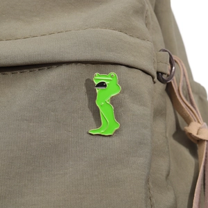 Gros plan d'une broche en émail de grenouille aux longues jambes sur un sac à dos vert olive