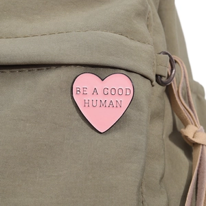 Dettaglio della spilla a cuore rosa con scritta Be A Good Human su borsa in tela oliva