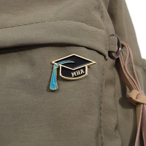 Macro shot of an MHA graduation cap enamel pin with blue tassel on olive green canvas