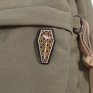 Detail view of gothic coffin enamel pin with red axe and geometric beehive pattern