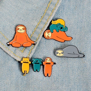 Close-up of sloth and koala enamel pins pinned on denim fabric showing metal textures