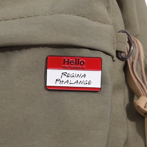 Macro view of Hello my name is Regina Phalange enamel pin on green canvas bag
