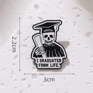 Macro shot of skull graduate enamel pin showing sizes 3cm and 2.2cm on white stone
