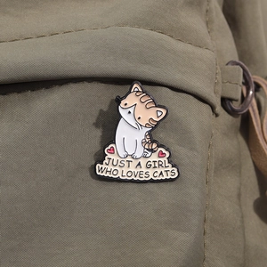 Detail of cute orange tabby cat enamel pin with hearts pinned on a green canvas backpack