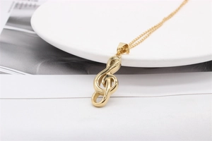 Detailed view of a golden music note pendant necklace resting on a white ceramic dish