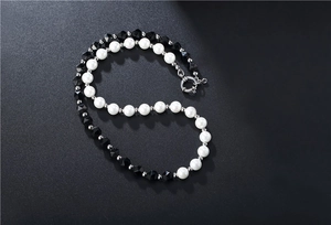 Détail du collier de perles noires et blanches avec fermoir argenté sur fond mat