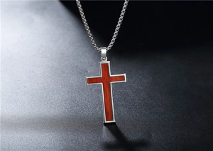 Detail of a stainless steel religious cross pendant with wood inlay on textured background