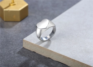 Polished silver heart signet ring displayed on a gray stone pedestal for a modern look
