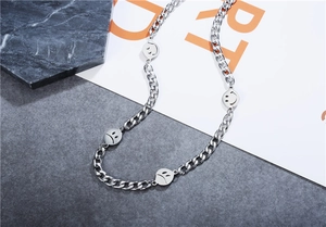 Detail of silver Cuban link necklace featuring engraved smiley face charms on stone texture