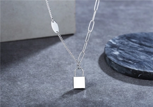 Close-up of asymmetric silver necklace with mixed paperclip chain and lock pendant