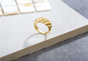 Detailed close-up of a golden croissant ring with elegant spiral texture on stone surface