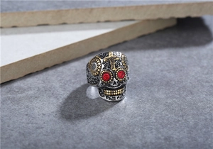 Vue détaillée d'une bague tête de mort punk avec yeux en gemme rouge et croix dorée