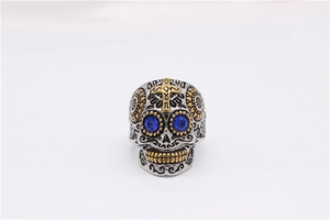 Gros plan de la bague tête de mort avec yeux en strass bleus et croix dorée