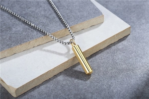 Macro detail of a minimalist gold cylinder pendant with silver steel box chain on stone