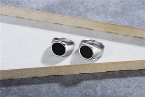 Close-up of two polished stainless steel signet rings with black enamel circular inlay
