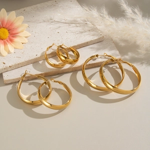 Three pairs of golden stainless steel hoop earrings in varied sizes on a minimalist stone base