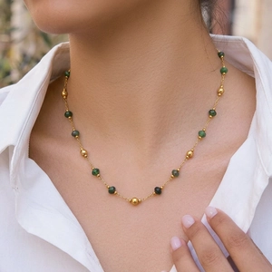 Macro detail of emerald-green faceted stone beads and polished gold beads on a necklace