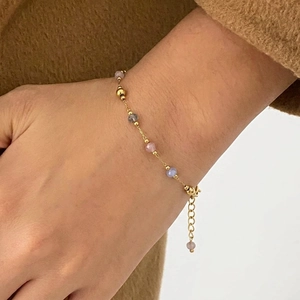 Detail of a delicate gold chain bracelet with colorful faceted beads on a person's wrist