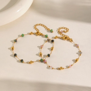 Close-up of golden chain bracelets featuring multi-colored faceted beads and lobster clasp