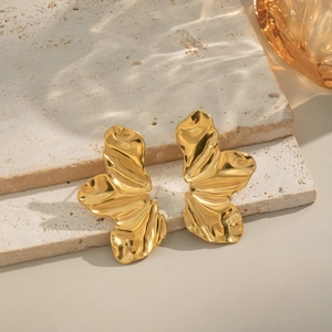 Détail des boucles d'oreilles pétales dorées avec texture ondulée sur socle en pierre