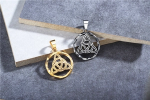 Macro shot of gold and silver Celtic Triquetra knot pendants on stone texture surface