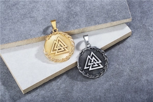 Macro detail of gold and silver Viking Valknut pendants on a textured stone surface