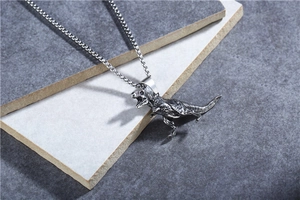 Detailed close-up of a vintage steel T-Rex dinosaur pendant on grey stone display