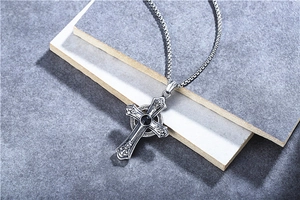 Macro view of vintage cross pendant with black stone and silver box chain on stone tiles