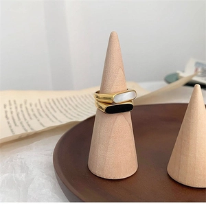 Detail of two geometric gold plated rings with black and white inlay on wooden stand