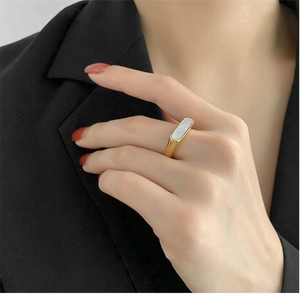 Detail of a geometric gold ring featuring a white shell inlay on a model's finger