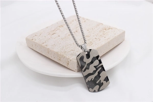Détail d'un pendentif camouflage rectangulaire sur une chaîne gourmette et socle en pierre