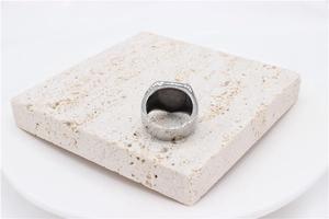 Close-up of wide silver stainless steel rock shield ring on a textured stone base