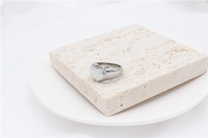 Detailed view of polished silver heart ring on beige travertine stone display