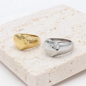 Minimalist gold and silver heart signet rings displayed on a textured stone base