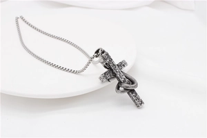 Dettaglio del ciondolo punk vintage con serpente avvolto su croce in acciaio
