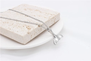 Pendentif queue de baleine poli sur une chaîne fine posé sur un support en pierre