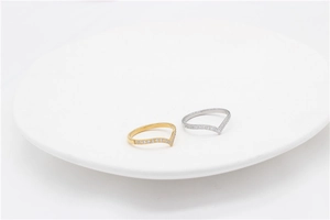Dettaglio di anelli a V color oro e argento con micro-pave su un piatto bianco