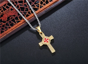 Makroaufnahme von Goldkreuz-Anhänger mit roter Emaille und keltischen Knoten an einer Kette