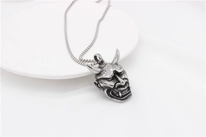 Macro view of Japanese Oni mask pendant with detailed fangs on a box chain necklace
