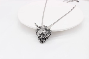 Detailed top view of a vintage silver Hannya mask pendant on a white round display