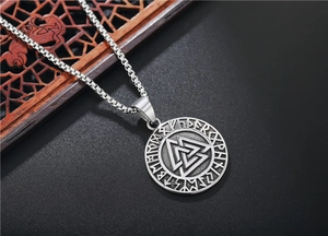 Detailed close-up of vintage Valknut pendant with runic alphabet on dark wood background