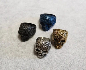 Dettaglio di quattro anelli a teschio punk gotico in blu, nero, oro e argento
