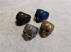 Dettaglio di quattro anelli teschio punk vintage in oro, argento, nero e blu con incisioni