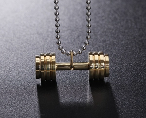 Macro d'un pendentif haltère doré avec chaîne à billes sur fond texturé