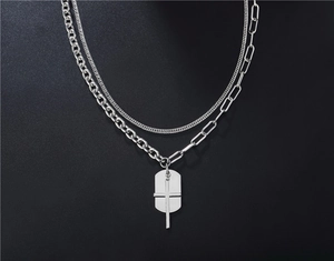 Dettaglio macro della collana punk argento con pendente a croce e piastrina metallica