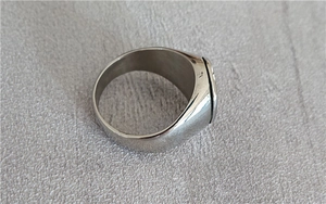 Close-up of industrial punk style stainless steel signet ring with wide band on stone surface