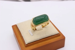 Detailed macro view of an emerald green rectangular gemstone set in a gold saddle ring band