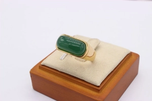 Macro shot of gold saddle ring with oval green emerald gemstone on jewelry stand