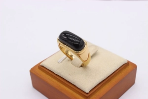 Macro shot of an oval black onyx gemstone set in a wide gold band on a jewelry stand